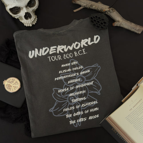 A dark charcoal gray t-shirt with white and light blue narcissus flower graphic with text reading 'UNDERWORLD TOUR 800 B.C.' and several underworld locations.