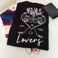 A black short-sleeve t-shirt laid flat on a white surface, featuring a white graphic print of two hockey helmets forming a heart, crossed hockey sticks, a hockey puck, and the text 'RIVALS to Lovers EST. 2019.'