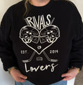 A person wearing a black crewneck sweatshirt, featuring a white graphic print of two hockey helmets forming a heart, crossed hockey sticks, a hockey puck, and the text 'RIVALS to Lovers EST. 2019.'